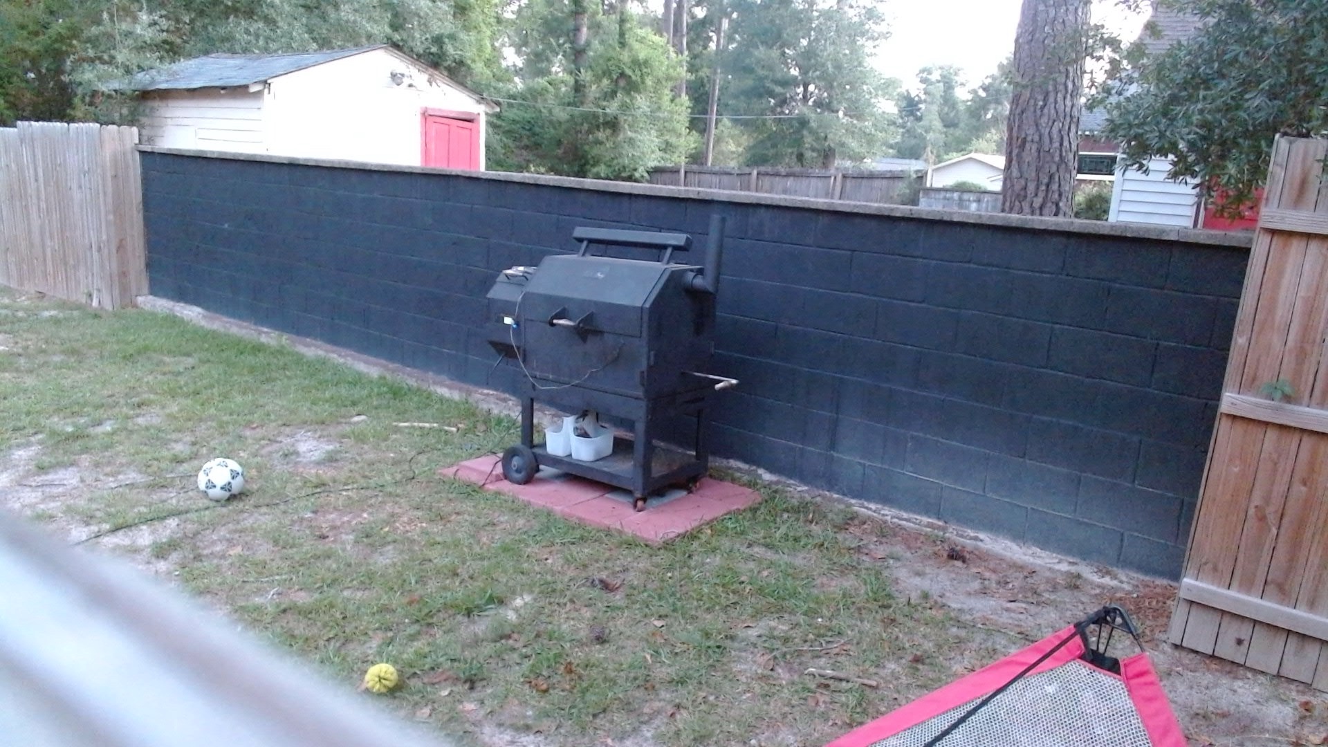 Early morning webcam view of the backyard smoker closed against a black wall, with FireBoard wiring visible and no obvious smoke or flame issue.
