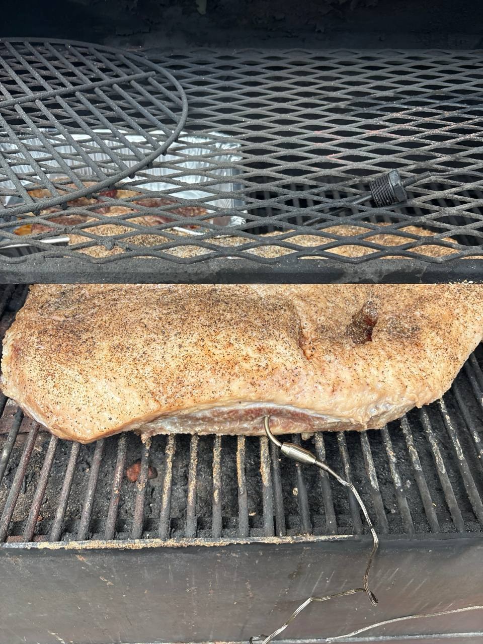 A seasoned brisket with a temperature probe just placed on the grill grate inside a smoker.