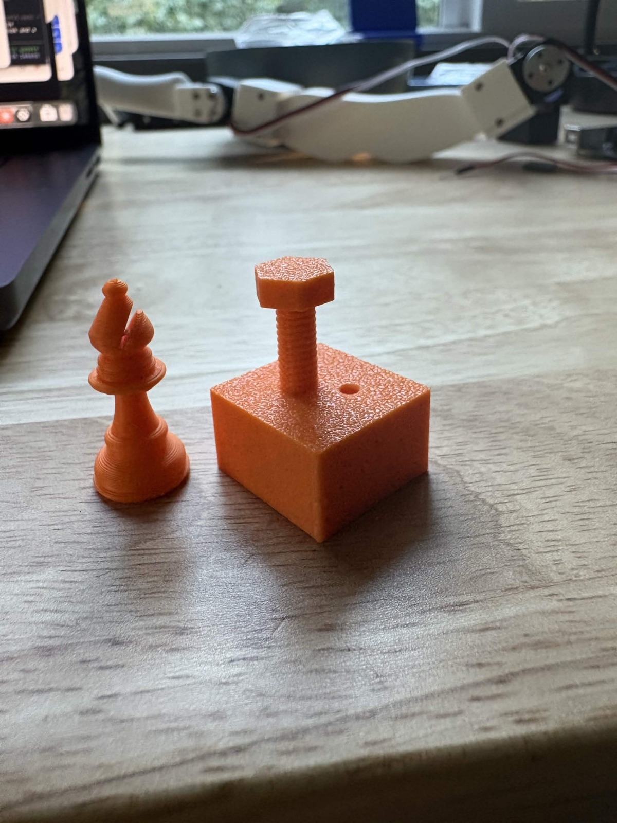 3D-printed orange bishop next to a printed block with a threaded screw in it
