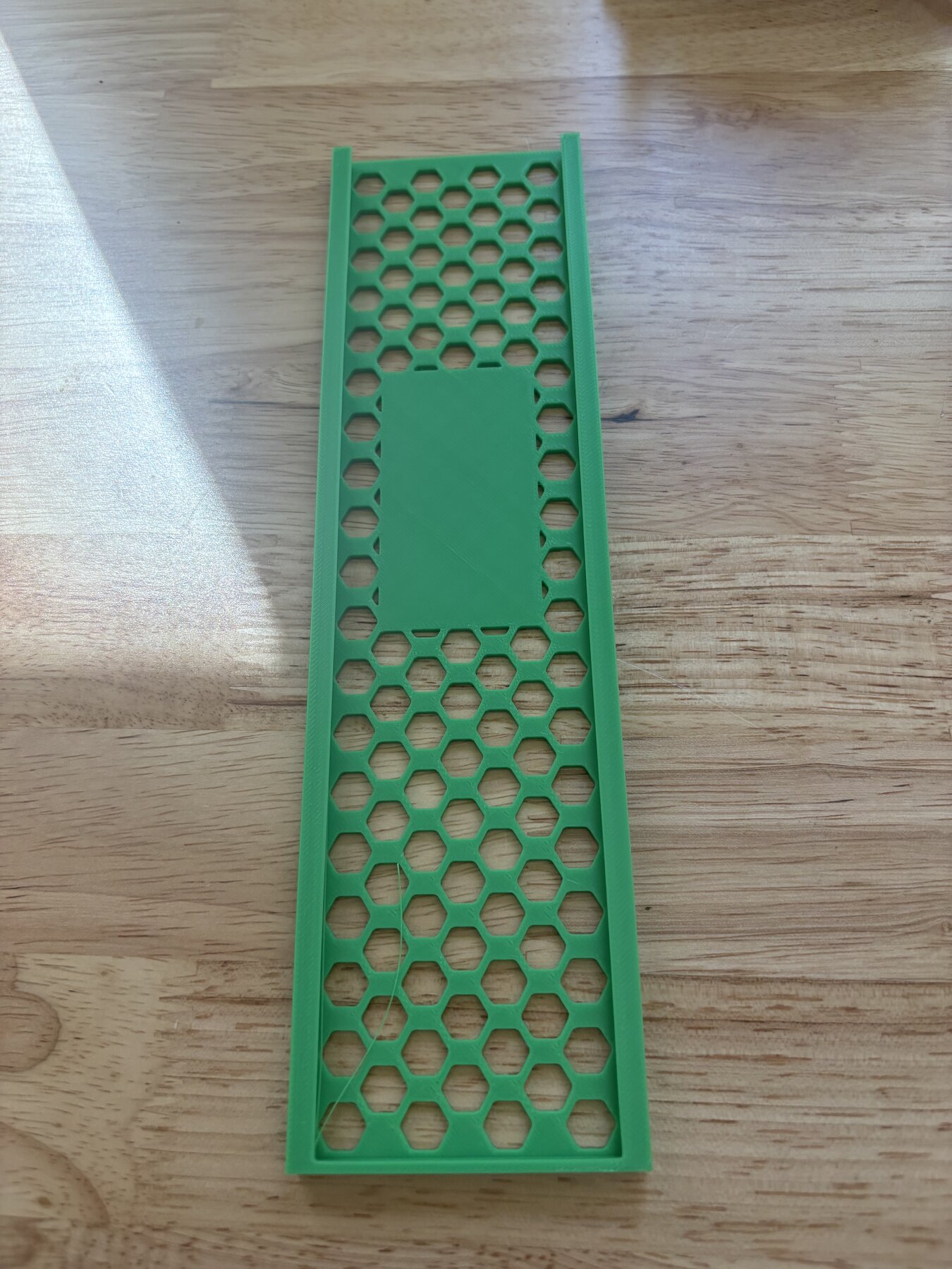 A green 3D-printed honeycomb tray resting on a wooden table
