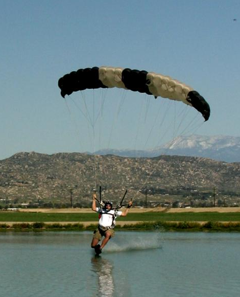 Justin swooping a small high-performance parachute across a pond with mountains in the background