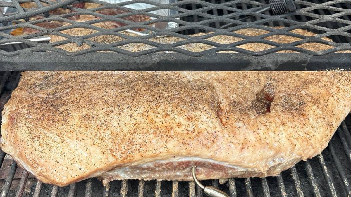 Seasoned brisket on a smoker grate with a temperature probe
